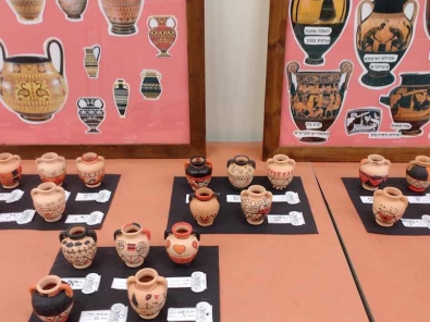 Greek mini urns made by sixth graders against a backdrop of posters showing classic Greek pottery techniques.